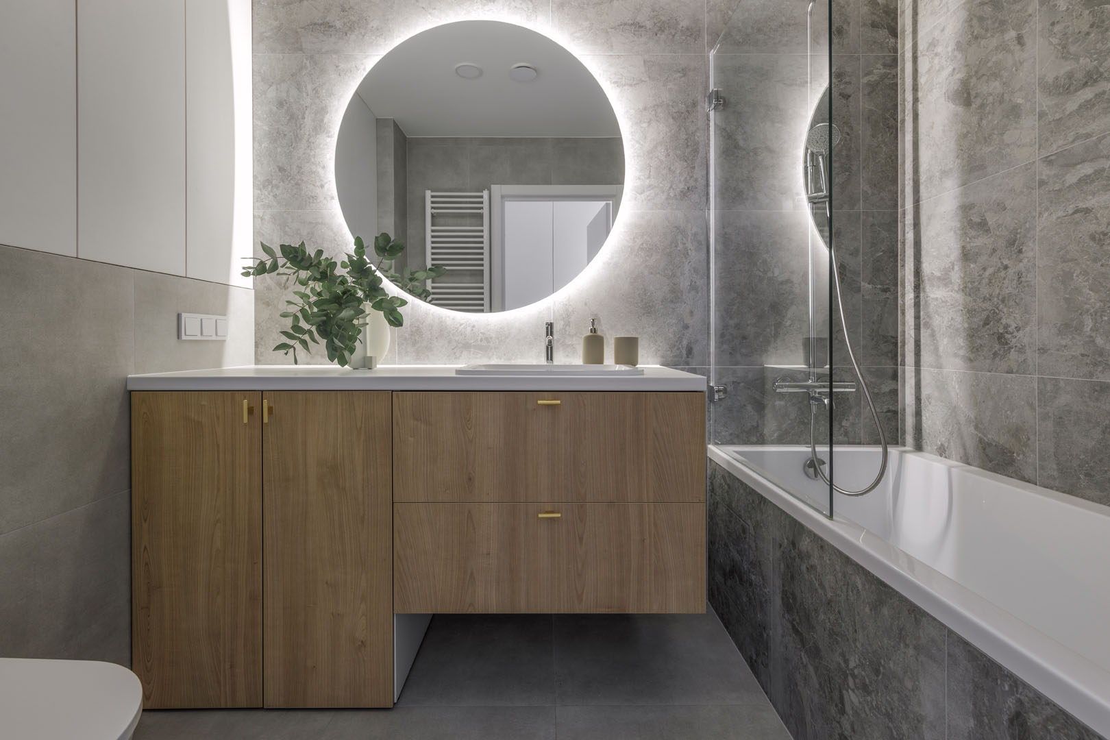 Modern minimalist bathroom interior design with wooden furniture, grey stone tiles, round mirror. Aesthetic simple interior design concept.